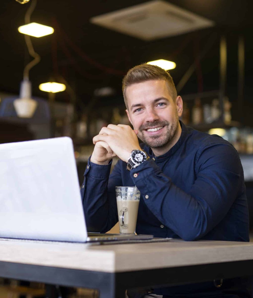 Portrait of smiling man sitting in a cafe bar with his laptop computer.